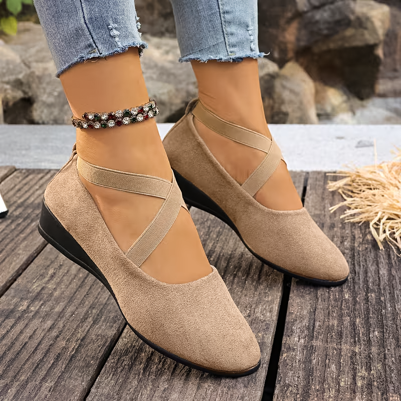 Beige wedge shoes worn with light blue jeans on a wooden surface.