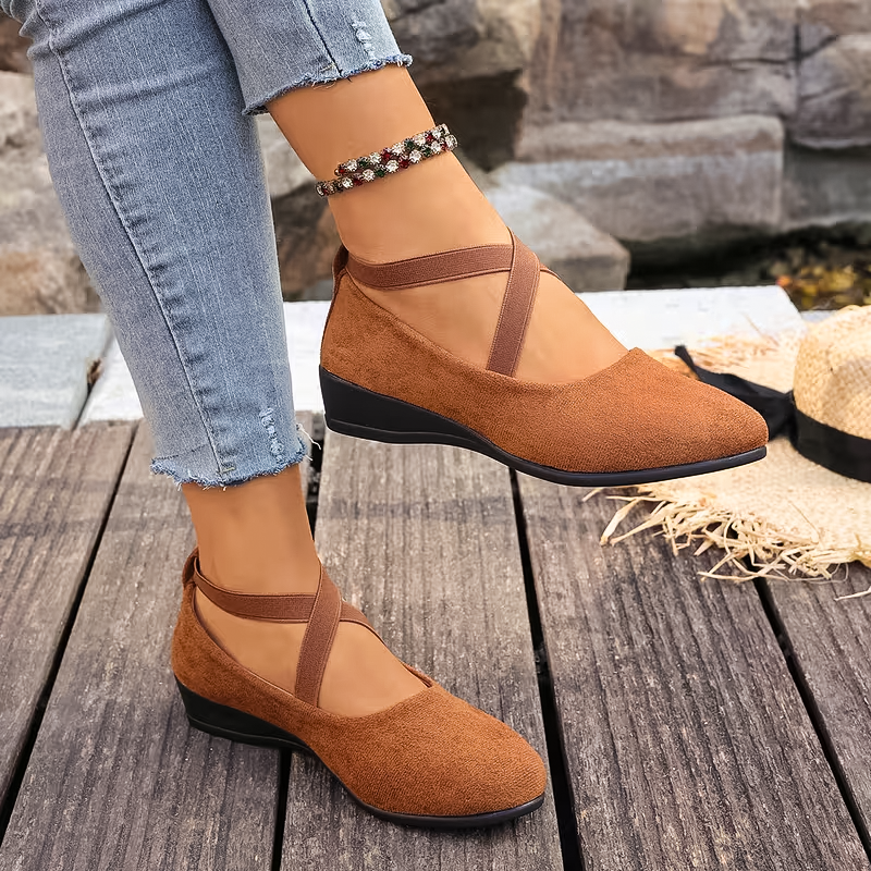 Brown suede shoes with black soles worn by a person on a wooden surface.