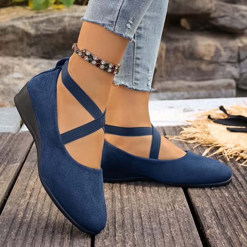 Navy blue shoes worn with denim jeans on a wooden floor.