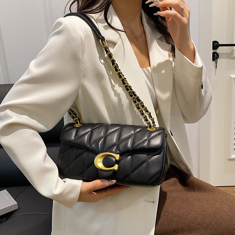 Person holding a black quilted handbag with gold chain strap and clasp.