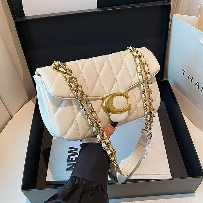 White quilted handbag with gold chain strap on a black box