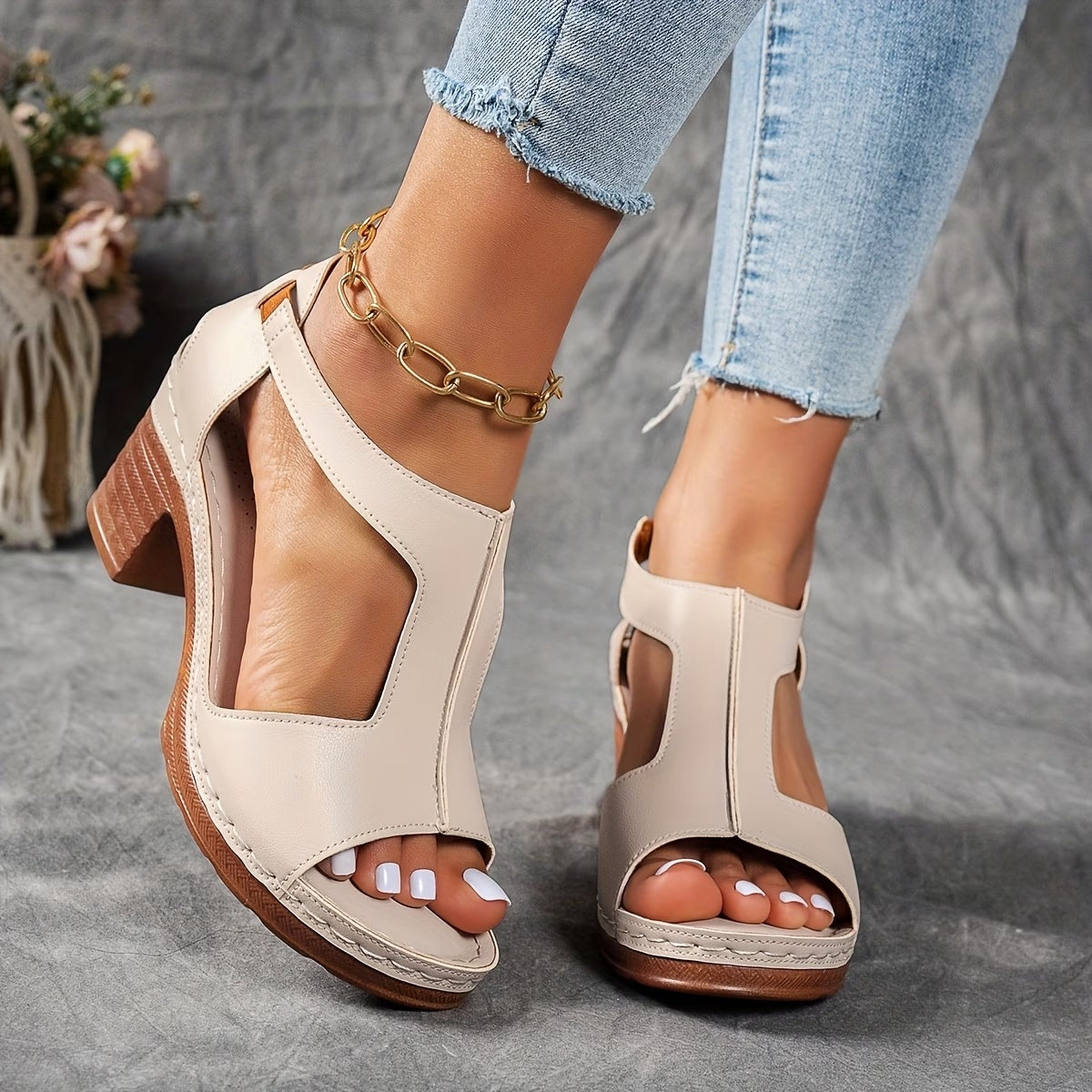 Beige open-toe sandals with wooden soles worn by a person on a gray surface.