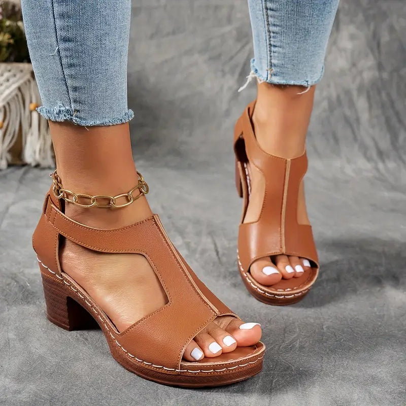 Brown open-toe sandals worn with light blue jeans on a gray surface.