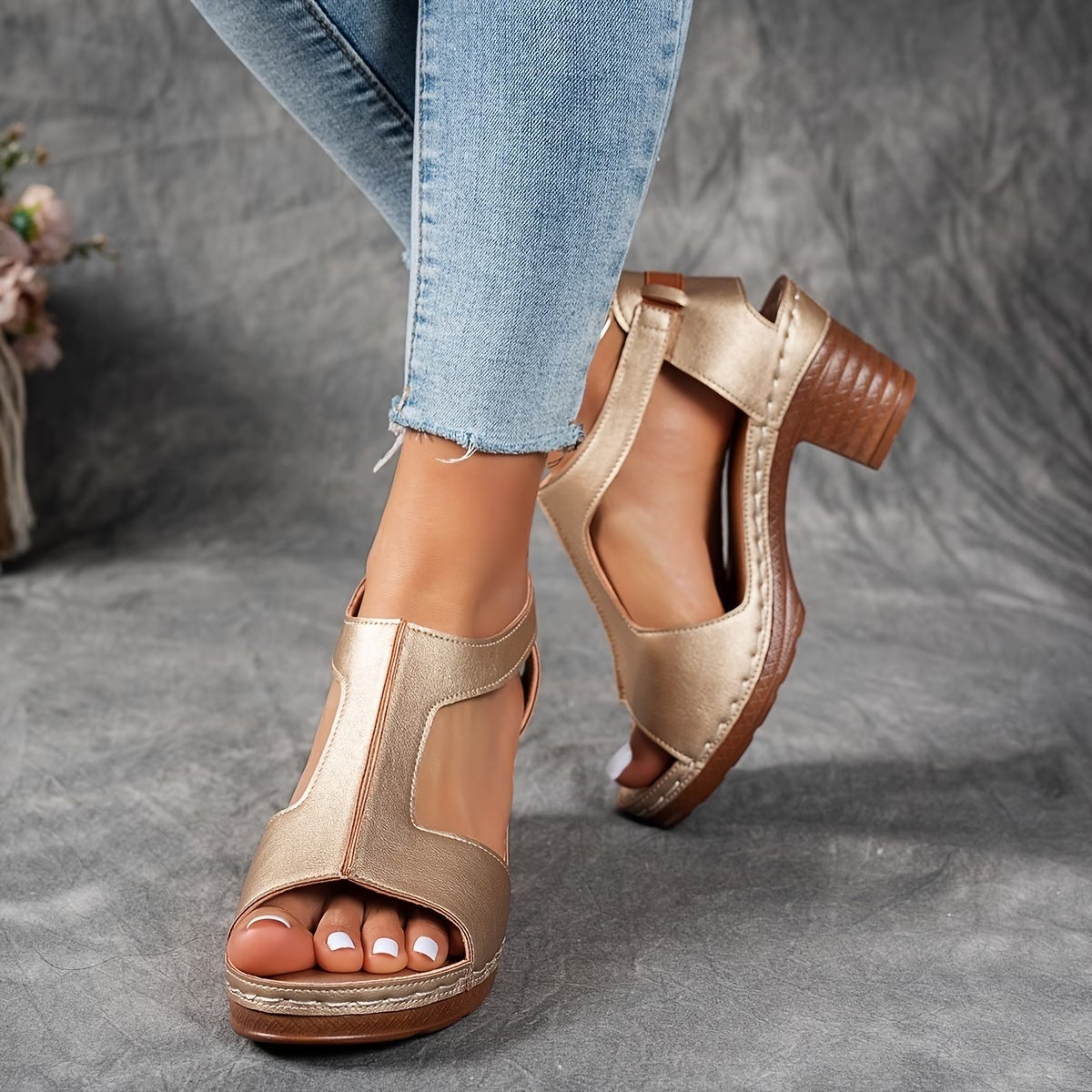 Gold open-toe sandals worn with light blue jeans on a gray surface.