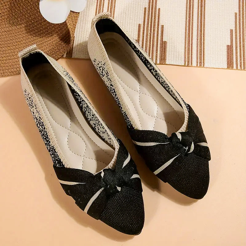 Black flat shoes with a bow on a beige surface