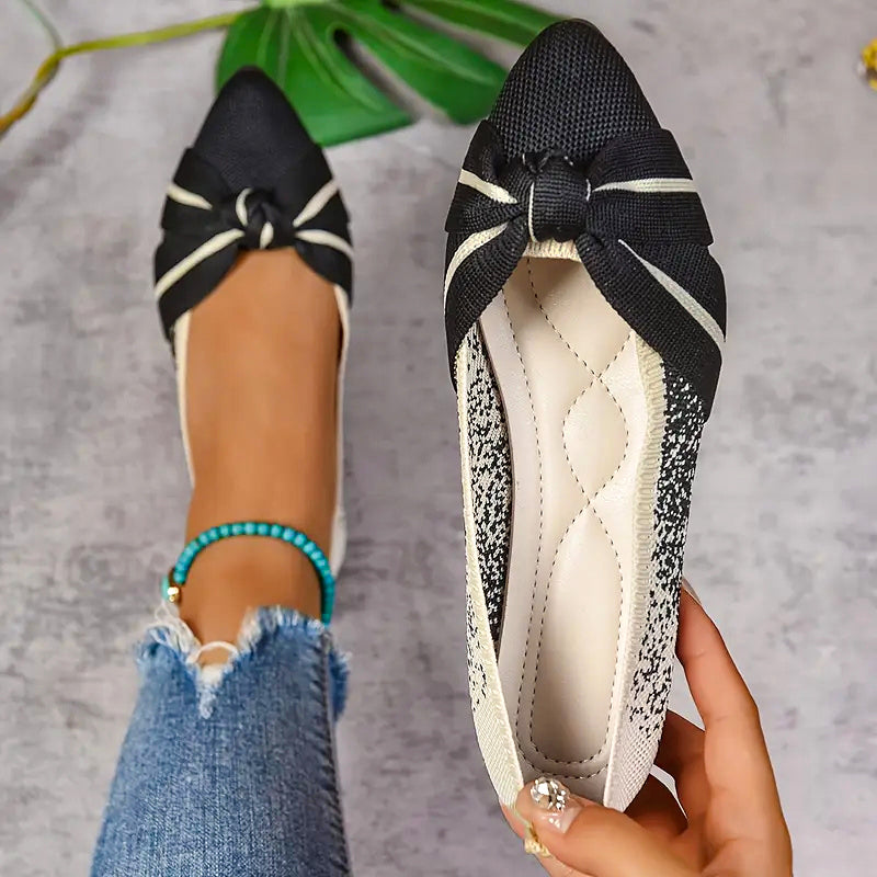 Black flats with bow detail worn by a person on a gray background