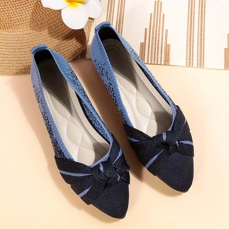 Pair of blue flat shoes with a bow on a beige surface.