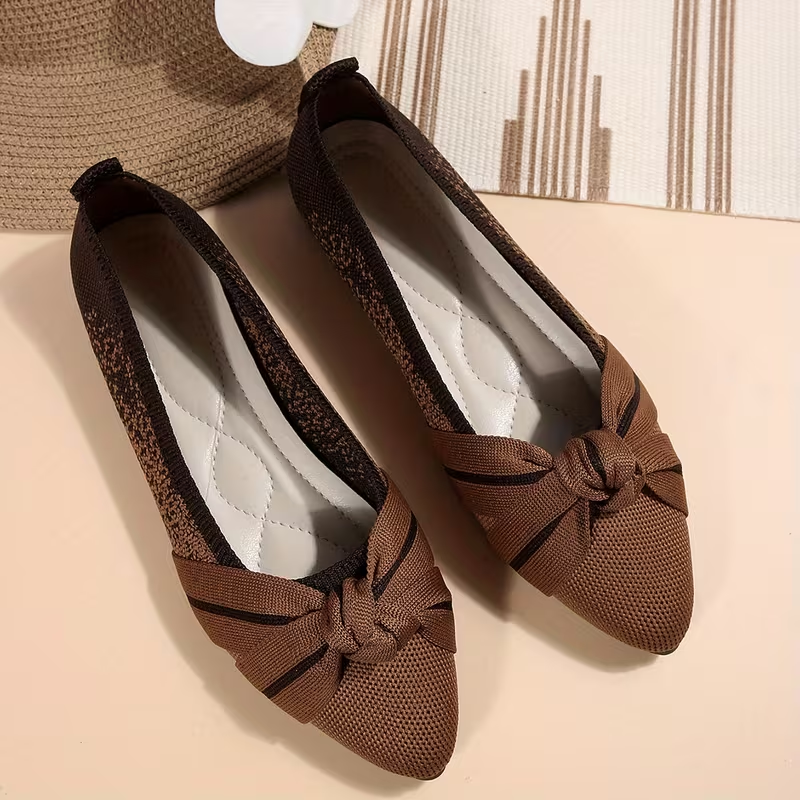 Brown flat shoes with a bow on a beige surface