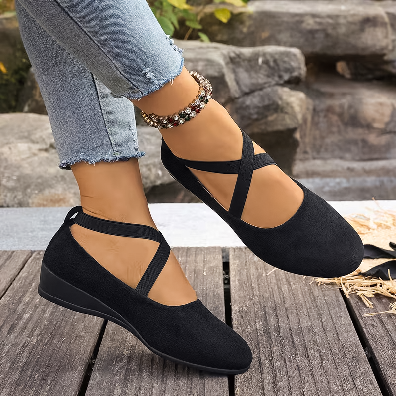 Black strappy flats worn with rolled-up jeans on a wooden surface.