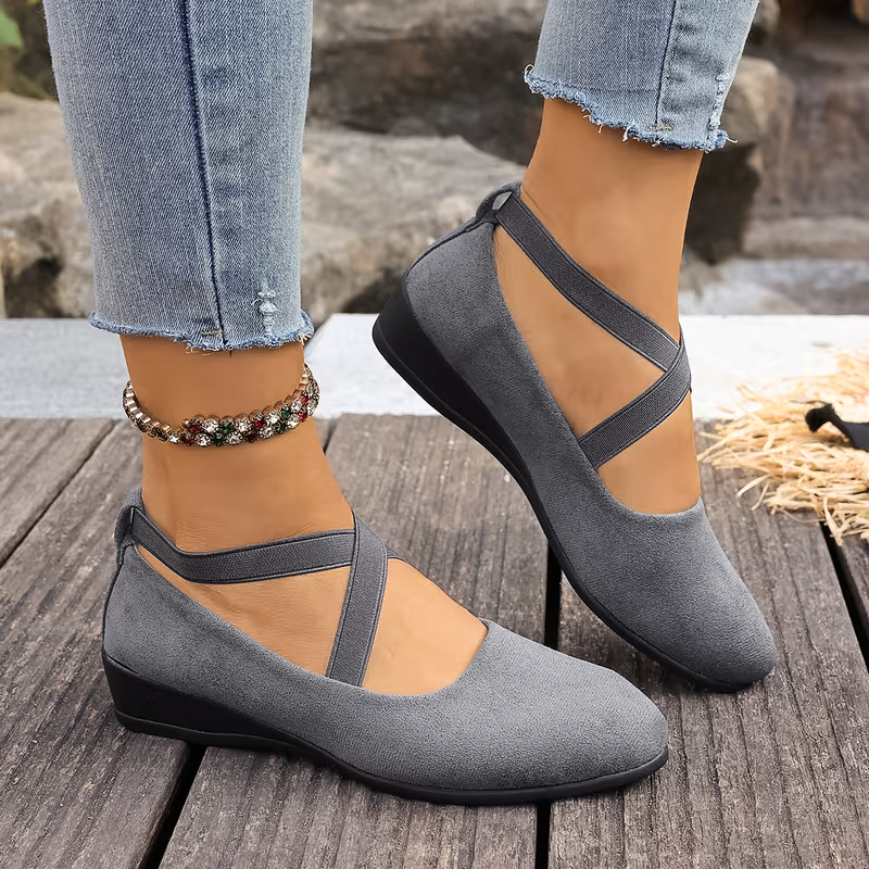 Gray shoes with black straps worn by a person on a wooden surface.