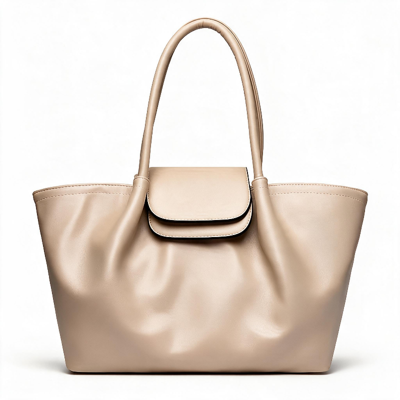 A large slouchy tote bag in a light beige or champagne-colored faux leather, featuring dual top handles and a matching flap closure on the front, set against a plain white background.