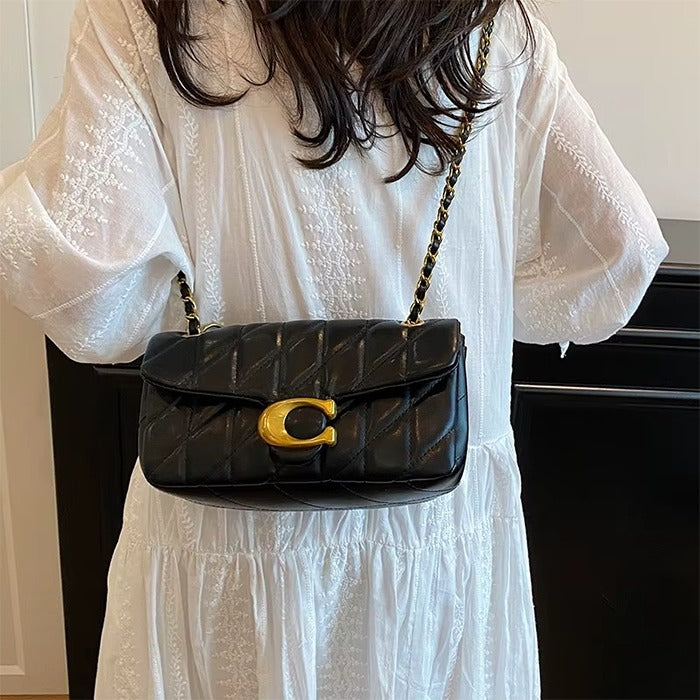Person wearing a white dress holding a black quilted handbag with a gold clasp.