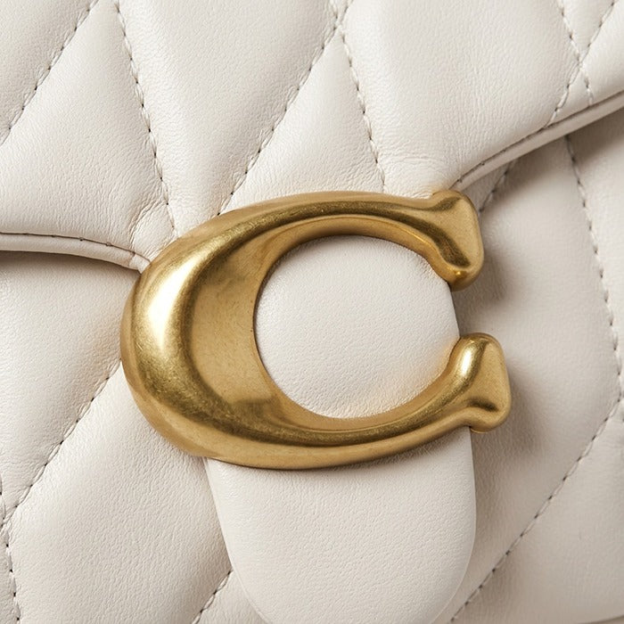 Close-up of a gold 'C' logo on a quilted white leather surface