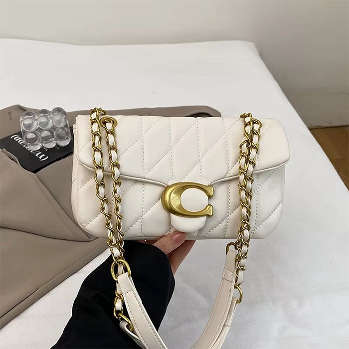 White handbag with gold chain and logo held by a person, with a beige bag and black card in the background.