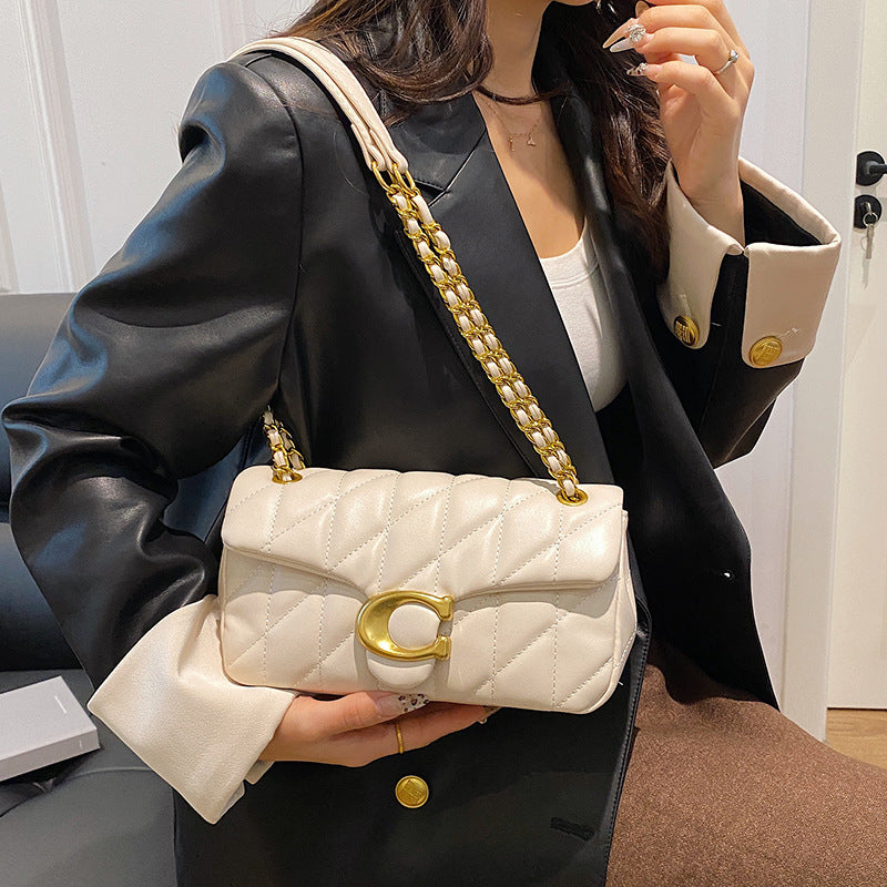 Person holding a white quilted handbag with gold chain and clasp.