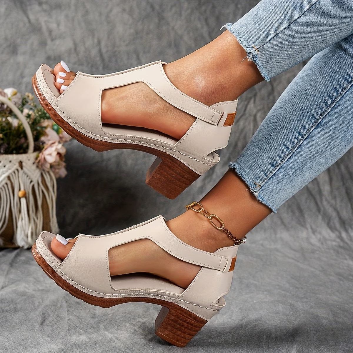 Beige sandals with wooden soles worn by a person sitting on a gray surface.