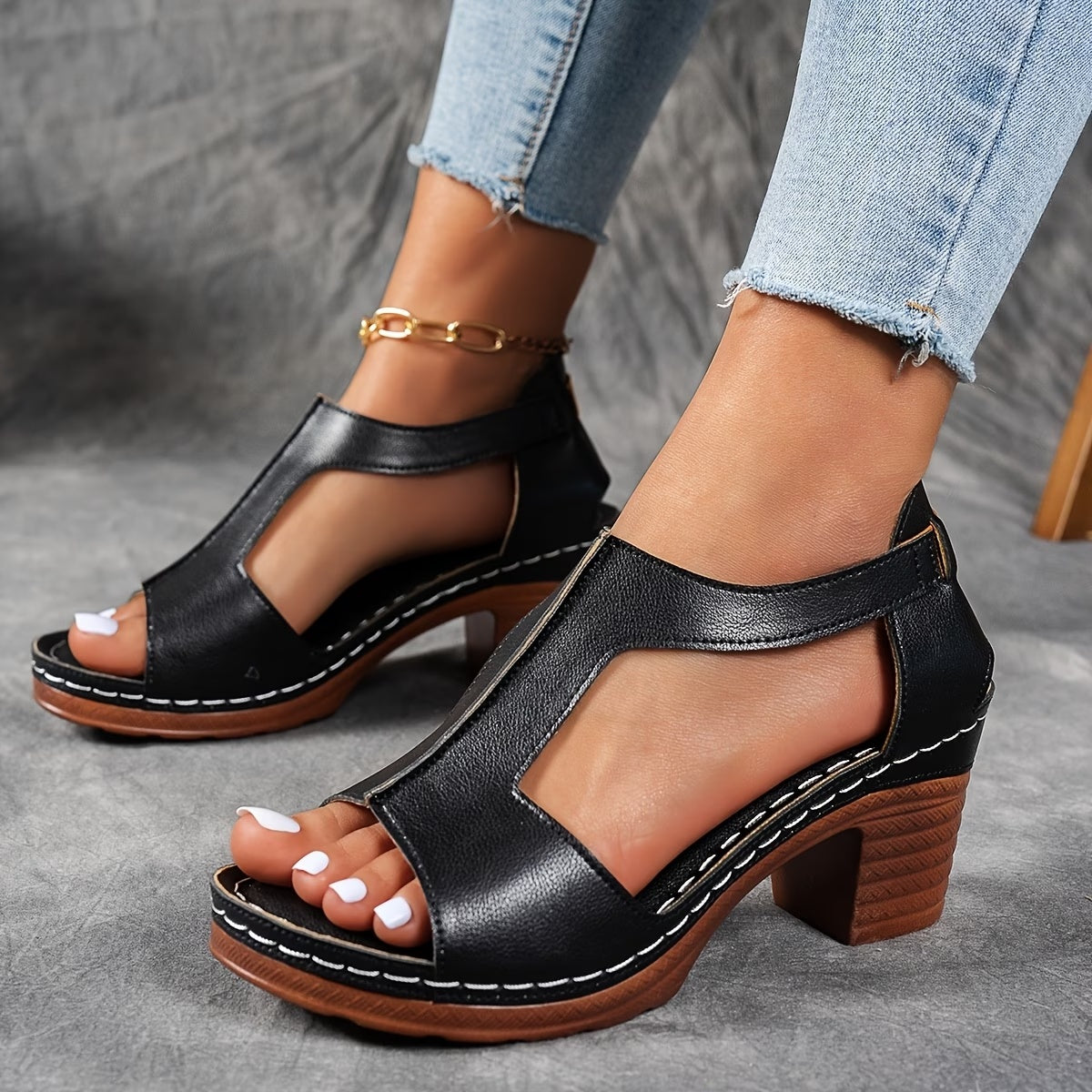 Black open-toe sandals with wooden block heel worn with light blue jeans on a gray surface.