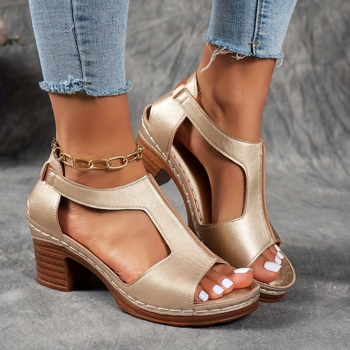 Gold open-toe high-heeled shoes worn with light blue jeans on a gray background