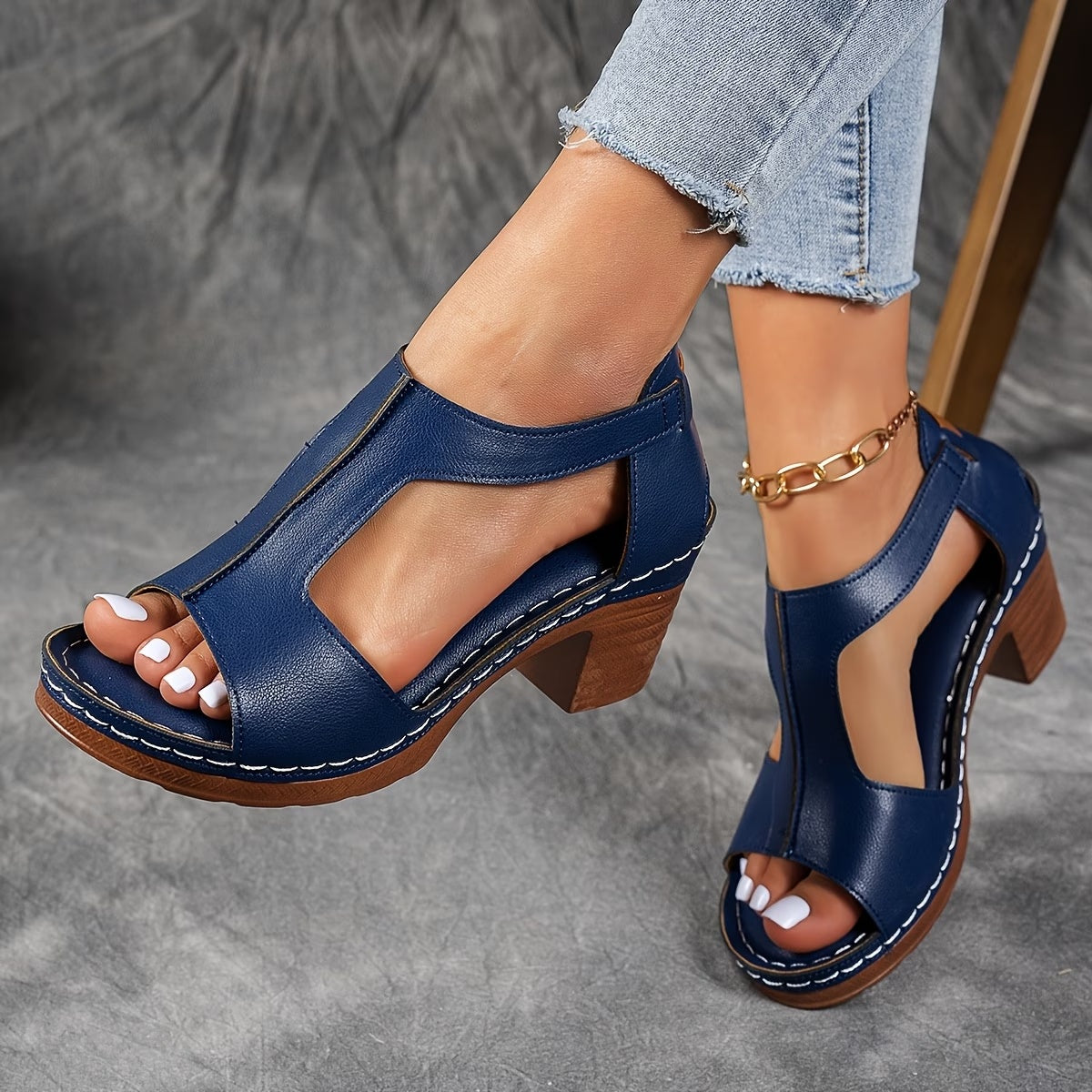 Blue sandals with wooden block heels worn by a person on a gray background