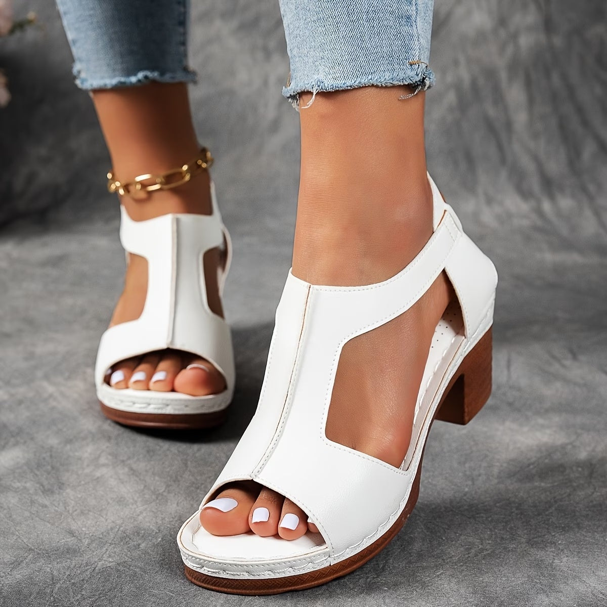 White open-toe sandals with brown soles worn by a person on a gray surface