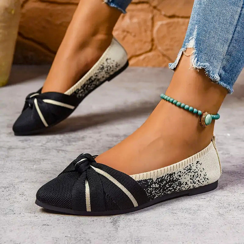 Black and white flat shoes worn with denim jeans on a concrete floor.