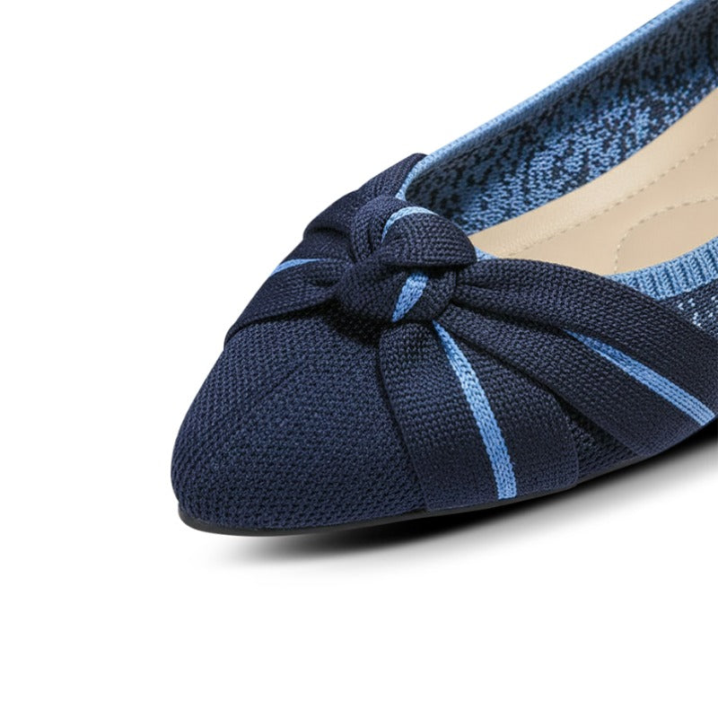 Navy blue flat shoe with a knotted design on a white background