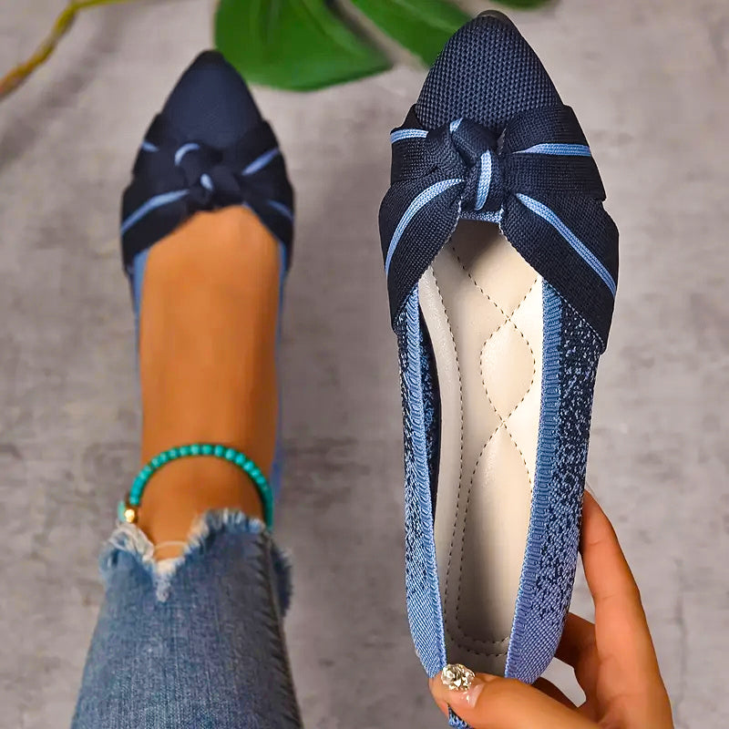 Blue flat shoes with a bow held by a hand, worn with ripped jeans.