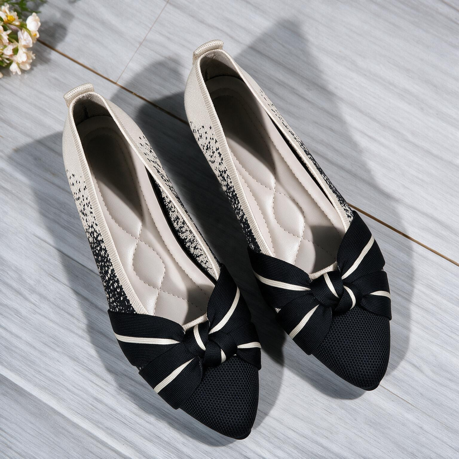A pair of women's low-heeled slip-on flats with a black and white speckled pattern, a black mesh toe cap, and a black ribbon bow with white stripes, displayed on a gray wood-look floor.