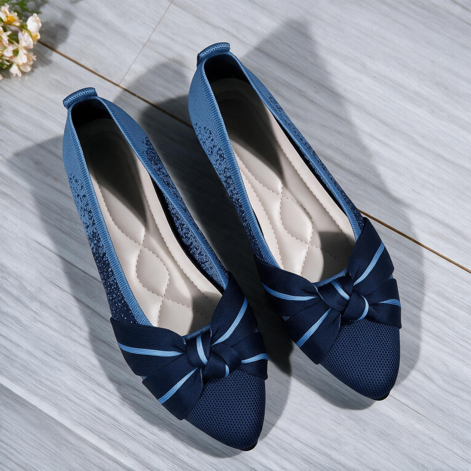 A pair of women's slip-on flats with pointed toes, featuring a textured navy blue mesh upper, a light blue side panel, and a matching navy bow with light blue stripes on the front. The shoes are displayed on a gray wood-look floor.